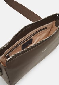 Borsa in pelle verde oliva con cerniera, l'interno ha un rivestimento beige chiaro e una piccola tasca. Presenta l'etichetta del marchio "JOOP!" all'interno.