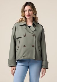 Olijfgroene, dubbelgeknoopte jas met grote bruine knopen, klepzakken en brede manchetten. Gemaakt van gladde stof met een losse pasvorm.