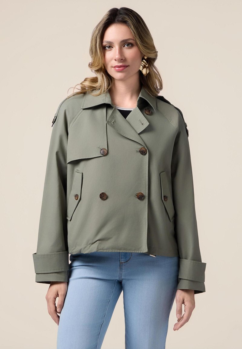 Olijfgroene, dubbelgeknoopte jas met grote bruine knopen, klepzakken en brede manchetten. Gemaakt van gladde stof met een losse pasvorm.