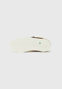 Shoe sole with a textured design; white rubber with a wavy pattern and a green accent. Upper portion is black, featuring a contrasting color edge.