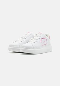 Bele teniske z rožnatimi detajli, izdelane iz gladkega materiala, z vezalkami, logotipom in debelim gumijastim podplatom za podporo.