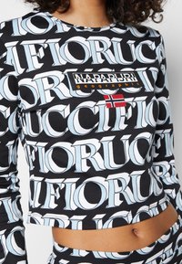 Top corto de manga larga con patrón en blanco y negro, con el texto grande "Napapijri geographic" y una pequeña bandera noruega en el pecho.