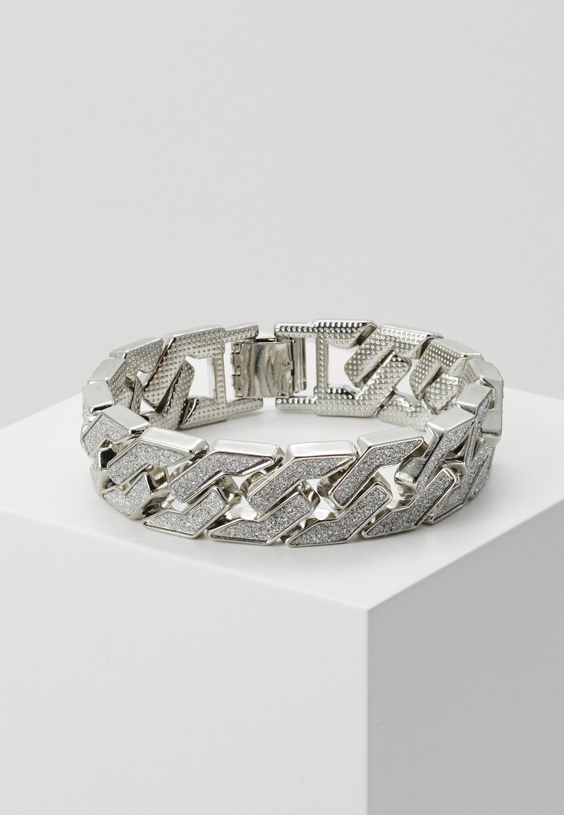 Sølv kjede armbånd med teksturerte og glatte ledd, som veksler mellom polerte og glitrende elementer, med en sikker lås.