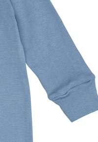 Garment lungo a maniche blu chiaro con polsini a costine, caratterizzato da una texture liscia e un design semplice. Il tessuto appare morbido e traspirante.