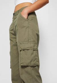 Pantalon cargo en mélange de coton vert olive avec une coupe décontractée, comprenant deux poches latérales et deux grandes poches cargo sur les cuisses.