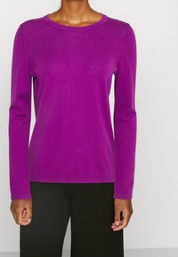 Top de punto de manga larga morado con cuello redondo y puños acanalados, combinado con pantalones de pierna ancha negros. Textura suave, ajuste casual.