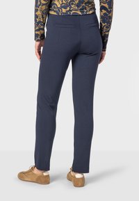 Navy blue pants with a slim fit, featuring belt loops and two back pockets. Fabric appears smooth with a slight stretch. Casual brown shoes visible.