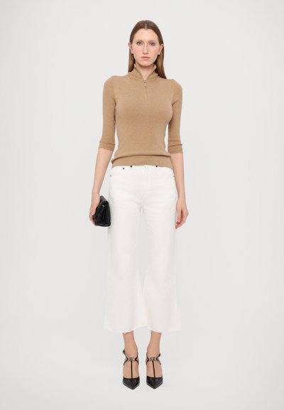 Haut en maille côtelée beige avec col haut, associé à un pantalon blanc à jambes larges. Un sac à main noir et des escarpins noir à bout pointu complètent le look.