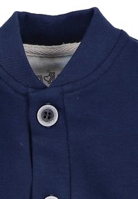 Granatowa bawełniana bluzka z okrągłym kołnierzem, z zapięciem na guziki. Gładka tekstura, prosty fason i kontrastowe podszewki widoczne od wewnątrz.