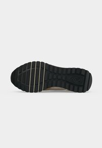 Semelle d'une chaussure noire avec des crampons profonds présentant des rainures horizontales et verticales et le nom de la marque « Gabor » embossé près du talon.