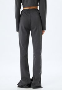 Donkergrijs, rekbare stoffen broek met een aansluitende taille en uitlopende zoom, met een gladde textuur en een eenvoudig ontwerp.