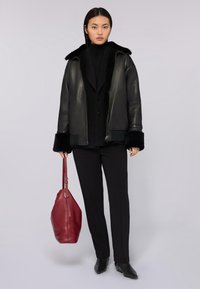 Czarna skórzana kurtka z kołnierzem z owczej wełny, połączona z czarnym golfem i dopasowanymi spodniami. Czerwona skórzana torba dopełnia stylizację.