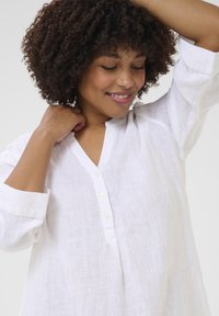 Camicia di lino bianca con scollo a V e patta dei bottoni. Caratterizzata da maniche lunghe e un tessuto leggero e testurizzato.