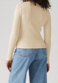 Top beige de manga larga con textura acanalada y diseño ajustado, combinado con vaqueros de mezclilla azul claro de pierna ancha, que cuentan con bolsillos traseros y un detalle de costura.