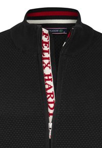 Maglione nero con zip e un motivo testurizzato, caratterizzato da un colletto a righe rosse e bianche e un nastro della zip a contrasto con il testo "FELIX HARDY".