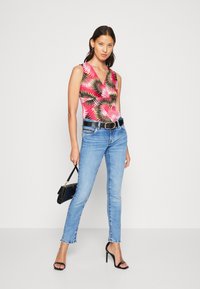 Bright pink sleeveless top with a palm leaf pattern, paired with light blue skinny jeans and black heeled sandals. Black belt and handbag.