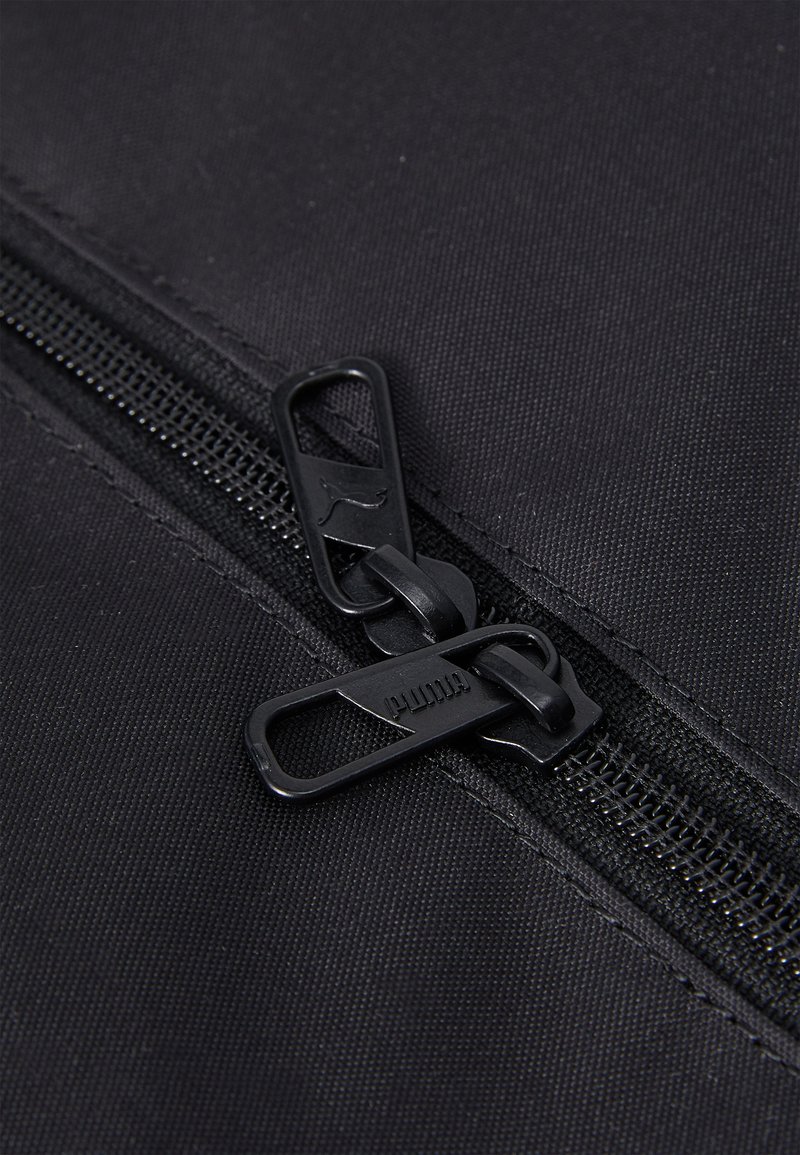 Zipper in tessuto nero con design a doppio cursore. Le linguette di apertura hanno una finitura opaca con un dettaglio del logo. I denti della zip sono visibili lungo il nastro.
