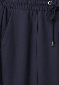 Mörkblå joggbyxor med elastisk midja, snörning och sidofickor; tillverkade av strukturerad tyg med en slät yta.