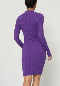 Robe ajustée à manches longues de couleur violette avec une texture côtelée, un col haut et une longueur mi-cuisse. Pas de motifs visibles ni de détails en métal.