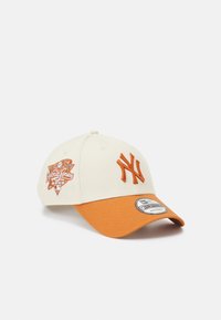 Cream baseball cap with an orange visor, featuring embroidered logo and graphics on the front. Cotton material, structured design.