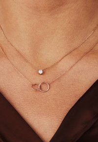 Colliers en or rose superposés présentant un pendentif circulaire et une seule pierre précieuse, mettant en valeur des chaînes délicates et des textures lisses.