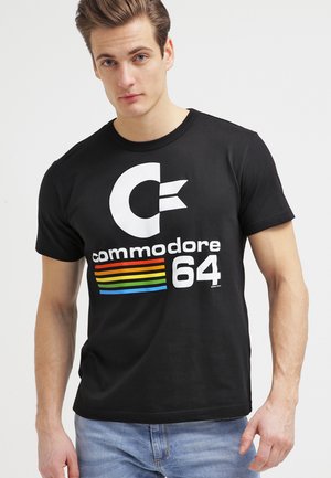 Sort bomulds-T-shirt med et stort hvidt "C" logo, "commodore" tekst og flerfarvede vandrette striber over "64." Korte ærmer, rund hals.