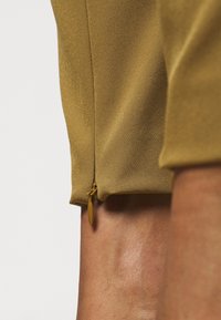 Hnědý detail oděvu se zipem ukazuje hladký, texturovaný materiál s rafinovaným povrchem a jemným leskem na lemu.