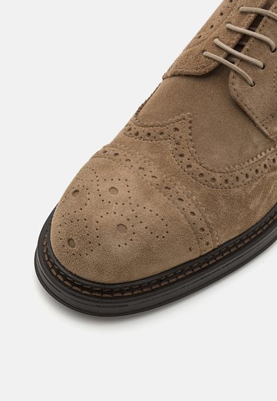 Brown suede dress shoe with brogue detailing, a rounded toe, and a contrasting black sole. Features are stitching and small perforations.