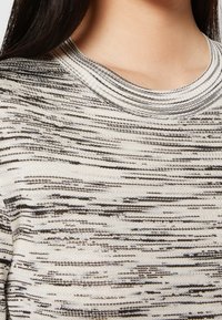 Stickad tröja med ett texturerat mönster i beige och mörka ränder. Har en rundad halsringning och mjukt tyg.