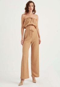 Beżowy, dwuczęściowy zestaw składający się z topu bez ramiączek z falbaną oraz spodni o wysokim stanie i szerokich nogawkach z troczkiem. Gładki, teksturowany materiał.