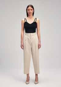 Top nero a righe con spalline sottili, abbinato a pantaloni beigi a vita alta, caratterizzati da una vestibilità sartoriale e una lunghezza corta, completato da tacchi.