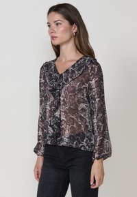 Blusa trasparente con motivo stampa serpente in tonalità di nero e beige. Presenta un collo a V, dettaglio frontale arricciato e maniche lunghe e gonfie.