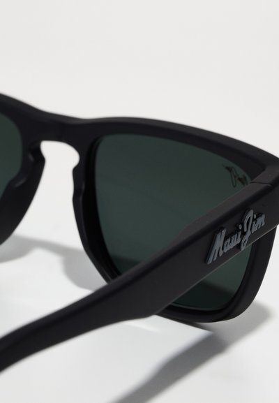 Svarta plastsolglasögon med mörkgröna linser, vinkelrätt design och präglad "Maui Jim"-logotyp på skalmen. Matt finish med lätt textur.