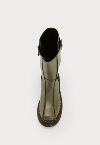 Botte en cuir vert olive avec semelle noire et coutures orange, vue de dessus, montrant la fermeture éclair et la boucle sur le côté.