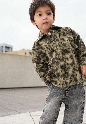 Veste verte à motif léopard, avec de gros boutons et une poche poitrine, associée à un jean gris clair déchiré.