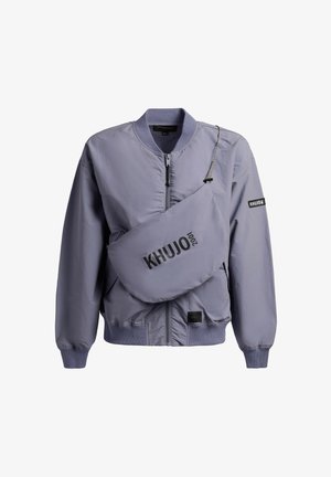 Vaaleanpunertava bomber-takki, jossa vetoketju edessä, ja siihen sopiva olkalaukku, jossa rintakehässä teksti "KHUJO 2001".