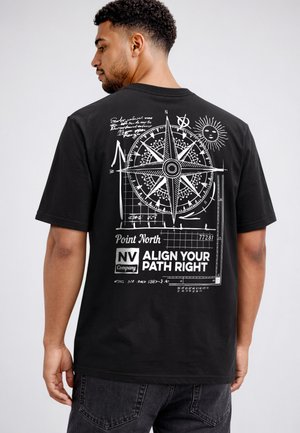 Man wearing black T-shirt with white compass design, sun graphic, and text "Point North NV Company Align Your Path Right" on the back.