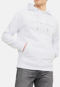 Hvid hættetrøje med en frontkangaroo lomme. Har et sort logo-tekstdesign. Blødt stof, ribbede manchetter og bund.