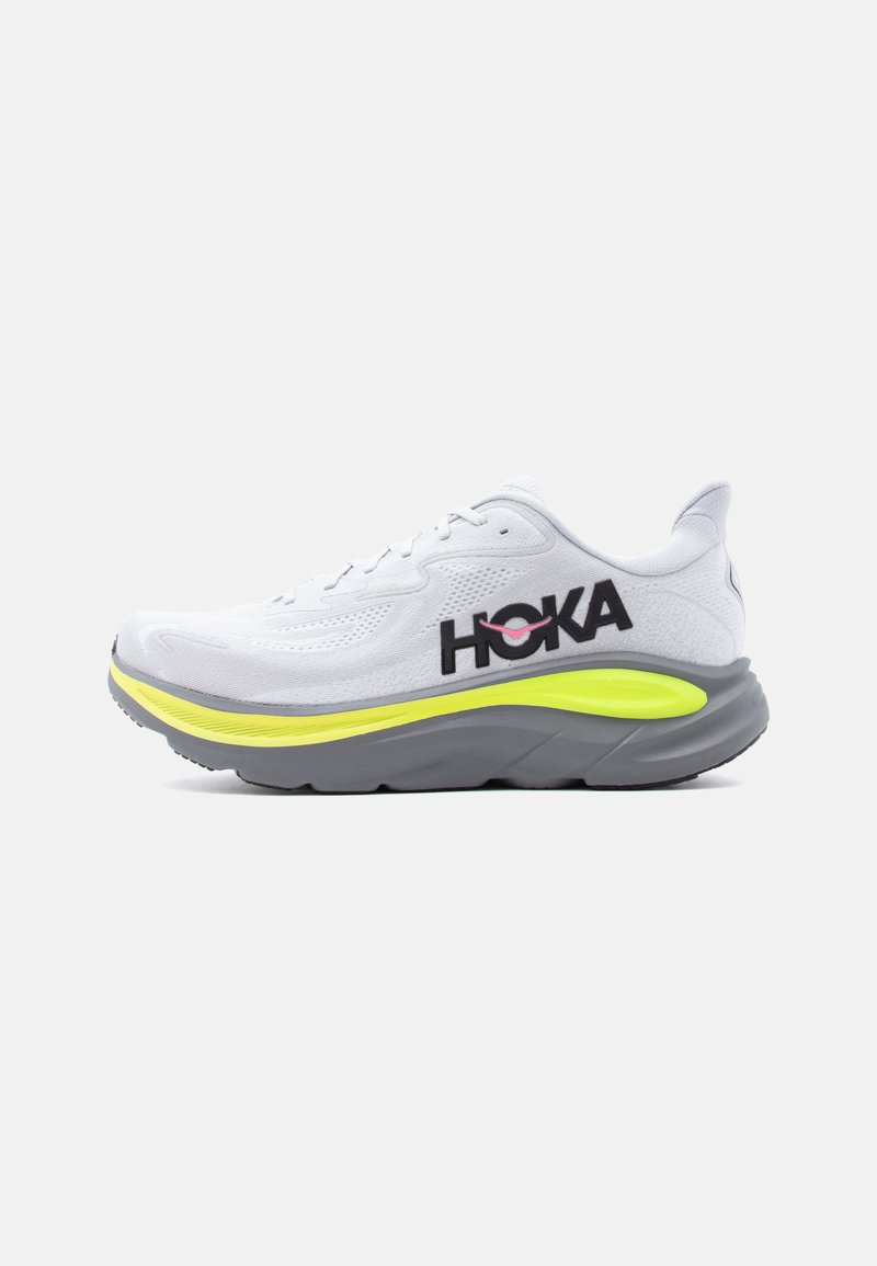 Witte hardloopschoen met bovenwerk van mesh, neongele middenzooldetail, grijze buitenzool en zwart "HOKA"-logo aan de zijkant.