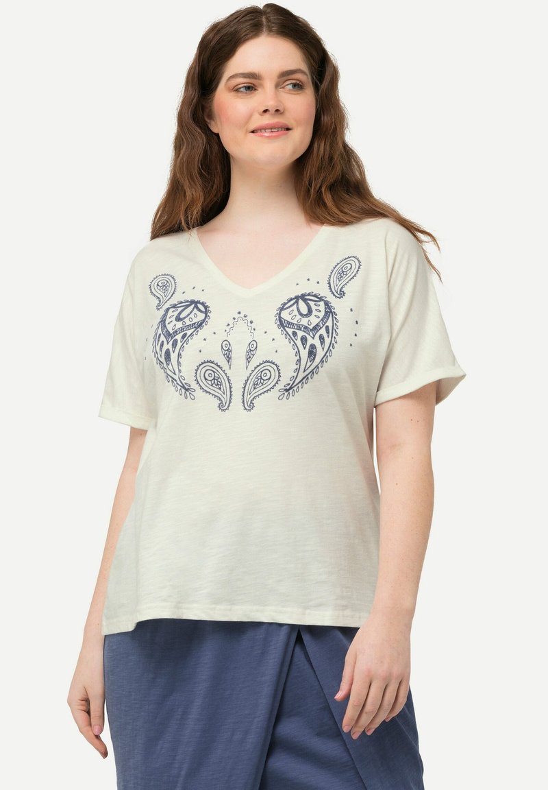 Camiseta de manga corta color crema claro con escote en V, que presenta un estampado de cachemir azul marino en el centro. Textura suave, corte holgado.