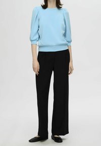 Suéter azul claro con mangas abullonadas y dobladillo acanalado, combinado con pantalones negros de pierna ancha. Textura suave en todo. Zapatos planos negros.