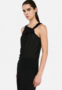 Black sleeveless top with a knot detail at the shoulder and a shimmering accent on one strap. Made of smooth, lightweight fabric.