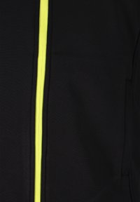 Giacca sportiva nera con zip gialla centrale, texture liscia e design minimalista con tasche laterali.