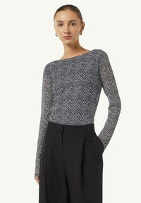 Langarm-Oberteil mit einem marineblauen und weißen Zickzackmuster, aus einem leichten Stoff gefertigt. Kombiniert mit hochtaillierten schwarzen Hosen.