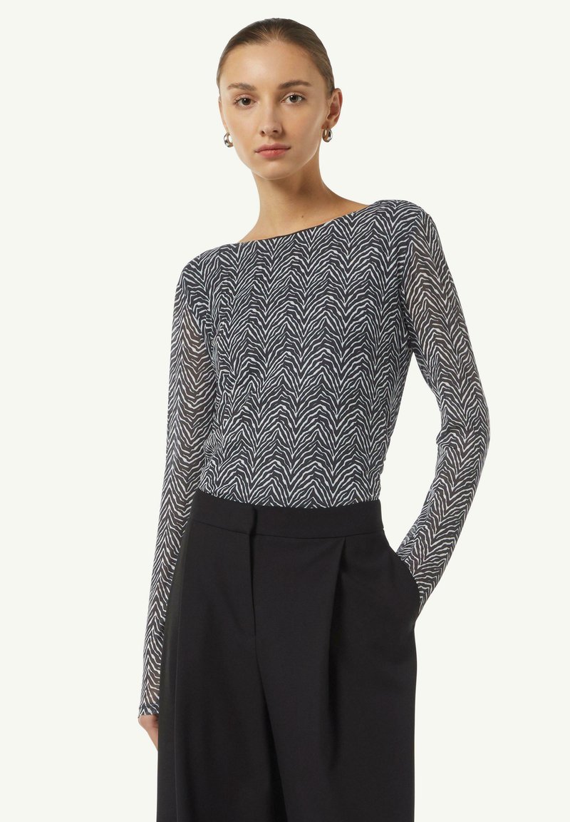 Langarm-Oberteil mit einem marineblauen und weißen Zickzackmuster, aus einem leichten Stoff gefertigt. Kombiniert mit hochtaillierten schwarzen Hosen.