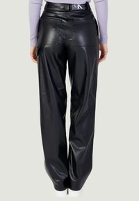 Zwarte neplederen broek met een losse pasvorm, uitgerust met achterzakken en een hoge tailleband. Zichtbare witte sneakeraccenten bij de enkel.