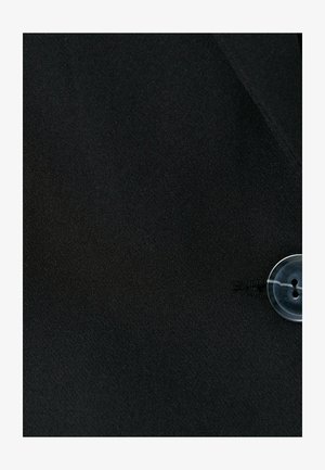 Musta kangas, jossa on sileä pinta, sisältää läpinäkyvän napin. Viimeistelty malli, jossa on hienovarainen kiilto ja klassinen siluetti.