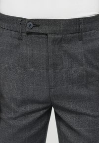 Graue Karo-Hosen aus leichtem Stoff; mit flachem Bund, Fronttaschen und einem einzigen Knopfverschluss am Bund.