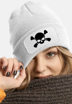 White knit beanie with a black skull and crossbones graphic. Textured fabric, rolled cuff design, worn tilted to one side.