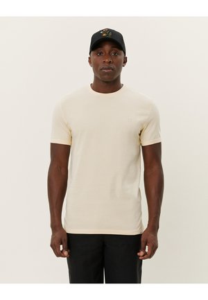 Cremfarbene T-Shirt mit kurzen Ärmeln im taillierten Design, aus weichem Stoff mit Rundhalsausschnitt. Getragen mit einer schwarzen Kappe mit besticktem Detail.